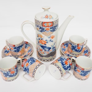 Könnte beinhalten: Ein weißes Porzellan-Tee-Set mit einem blauen und orangefarbenen Blumenmuster. Das Set enthält eine Teekanne, sechs Tassen und sechs Untertassen.