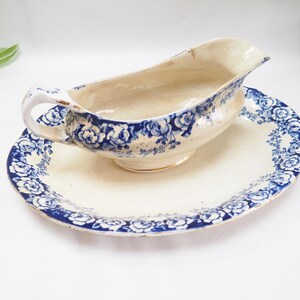 May include: A vintage white gravy boat with a blue and white floral pattern. The boat is sitting on a matching saucer.