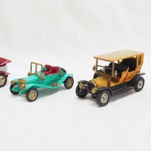 May include: Four vintage toy cars in various colors, including red, white, green, and yellow. The cars have detailed features, such as open tops, wooden accents, and spoke wheels. The cars are arranged on a white surface.