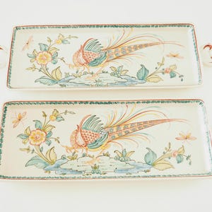May include: Two rectangular ceramic serving trays with decorative handles. Each tray features a colourful pheasant with a long tail, surrounded by floral designs in shades of green, yellow, and pink.