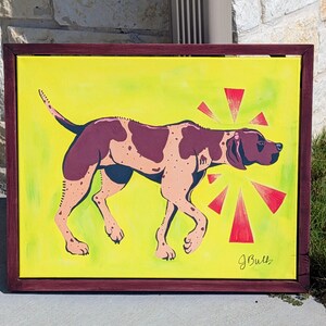 Puede incluir: Pintura enmarcada de un perro en tonos marrones y beige sobre un fondo amarillo. Formas de estrella rojas emanan de la cabeza del perro. El marco es de color burdeos oscuro. La firma del artista, "J. Bull", está en la esquina inferior derecha.