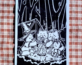 Könnte beinhalten: Ein schwarz-weißer Linoldruck auf Papier, der vier anthropomorphe, katzenartige Wesen zeigt, die um ein Lagerfeuer in einem Wald versammelt sind. Eine Figur trägt einen spitzen Hut, eine andere hat kleine Hörner, alles in einem kräftigen Stil.
