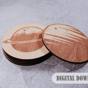 Puede incluir: Dos posavasos de madera con diseños de planetas grabados con láser. El posavasos de la izquierda presenta un planeta con anillos, mientras que el posavasos de la derecha tiene un diseño a rayas. El texto DESCARGA DIGITAL es visible en la parte inferior de la imagen.
