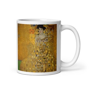 May include: White ceramic mug with a colorful image of a woman in a gold dress. The background is a mosaic of gold, yellow, and white squares.