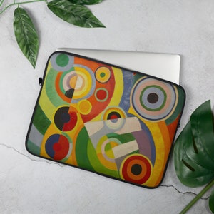 Pu&ograve; includere: Una custodia per laptop con un design geometrico astratto con cerchi e archi colorati. Il design ricorda un dipinto di arte moderna con una tavolozza di colori vibrante.