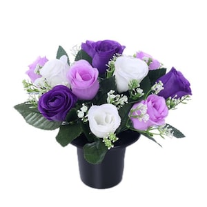 Pode incluir: Um arranjo floral com rosas roxas, lavanda e brancas. As rosas são dispostas com folhas verdes e pequenas flores brancas em um vaso cilíndrico preto. O arranjo está em um fundo branco.