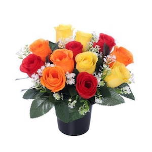 May include: A vibrant floral arrangement featuring a mix of red, orange, and yellow roses. The roses are arranged with green leaves and small white flowers in a black pot. A colorful and cheerful display.