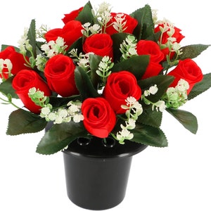May include: A bouquet of red roses with white filler flowers in a black plastic vase. The roses are artificial and the vase is designed for use in a cemetery.