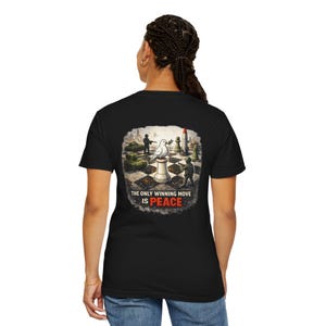 Może przedstawiać: Czarny t-shirt z grafiką na plecach przedstawiającą gołębia na figurze szachowej, otoczonego elementami wojskowymi. Tekst brzmi: "THE ONLY WINNING MOVE IS PEACE".