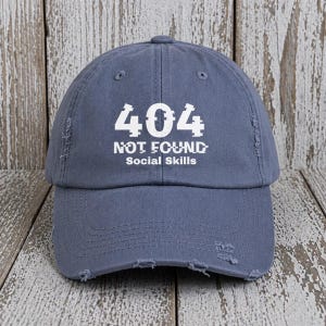May include: A distressed blue baseball cap with the text "404 NOT FOUND Social Skills" in white. The cap has a curved brim and a distressed, worn look.
