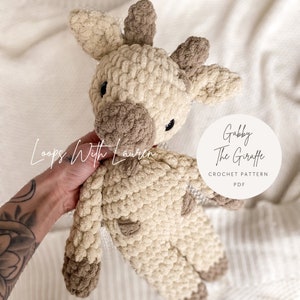 Könnte beinhalten: Ein gehäkeltes Giraffen-Amigurumi-Spielzeug in Beige und Braun mit dem Text "Gabby The Giraffe Crochet Pattern PDF" auf einem weißen Kreis.