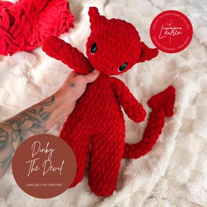 Op de afbeelding: Handgemaakte rode gehaakte duivelpop met zwarte ogen, hoorns en een staart. De tekst "Dinky The Devil" en "Crochet Pattern PDF" is zichtbaar op de afbeelding. De achtergrond is zacht en wit.