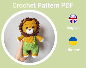 May include: Crochet pattern PDF for a lion amigurumi toy. The lion is wearing green overalls and has a brown mane. The pattern is available in English and Ukrainian.
