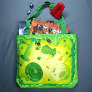 May include: Green canvas tote bag with a slime green design featuring a sword, a skull, a pouch, and dice. The bag has a green handle and is filled with books and dice.