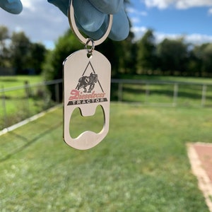 Può includere: Portachiavi apribottiglie in argento con un logo di trattore in bianco e nero e il testo "Dieselboss Tractor".