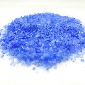 May include: A pile of small, iridescent blue glass shards. The shards are scattered on a white surface.