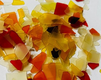 May include: A collection of colorful, translucent glass pieces in shades of orange, yellow, and red. The pieces are scattered on a white surface and appear to be broken or chipped.