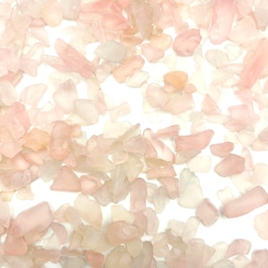 May include: A collection of pink and clear rose quartz chips. The chips are various sizes and shapes, and some have a translucent appearance.