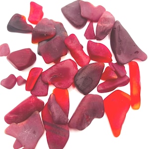 May include: A collection of red and purple sea glass pieces. The glass is smooth and has been tumbled by the ocean.