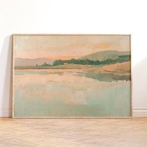 Puede incluir: Una pintura de paisaje enmarcada con un esquema de color azul claro y melocotón. La pintura representa un lago con un bosque en el fondo. La pintura está colgada en una pared blanca.