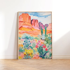 May include: A watercolor painting of a desert landscape with red rock formations and a variety of colorful flowers and plants. The painting is framed in a light wood frame.