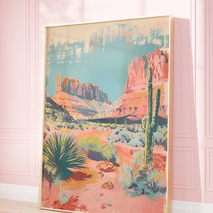May include: A framed print depicting a desert landscape with a large cactus in the foreground. The print is in a colourful, abstract style with shades of pink, orange, and blue.