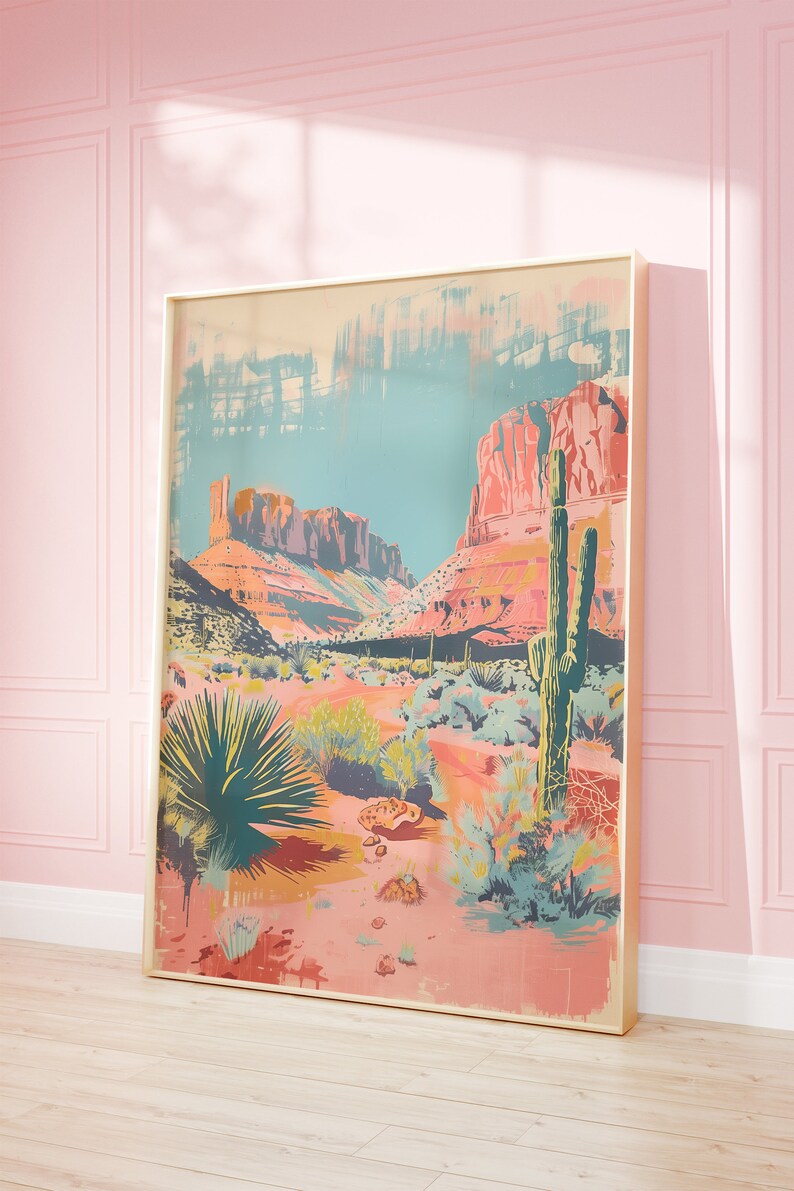 May include: A framed print depicting a desert landscape with a large cactus in the foreground. The print is in a colourful, abstract style with shades of pink, orange, and blue.