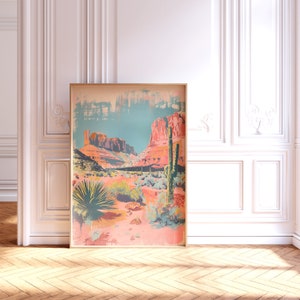 May include: A framed print depicting a desert landscape with red rock formations, a blue sky, and green cacti. The print has a vintage, faded appearance.