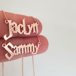 Puede incluir: Dos collares de tono dorado con los nombres "Jaclyn" y "Sammy" en fuente g&oacute;tica.