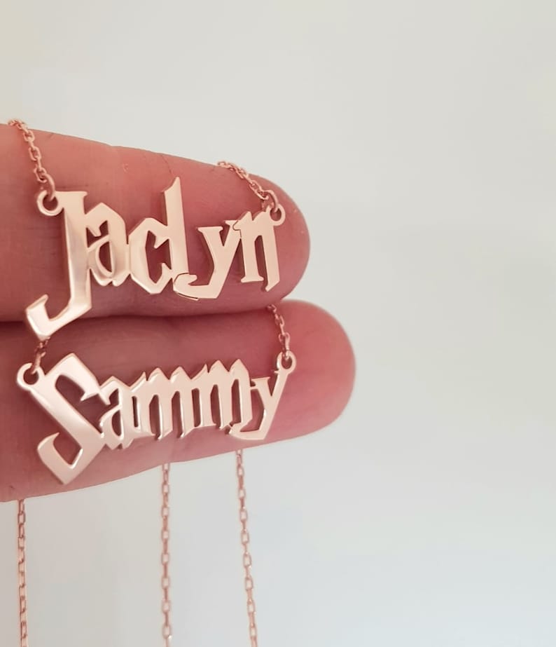 Puede incluir: Dos collares de tono dorado con los nombres "Jaclyn" y "Sammy" en fuente g&oacute;tica.