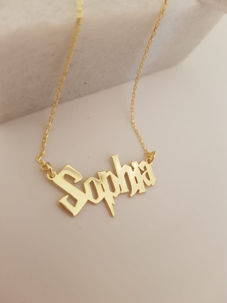 Puede incluir: Collar de oro con el nombre "Sophia" en fuente g&oacute;tica con un dise&ntilde;o de rayo.