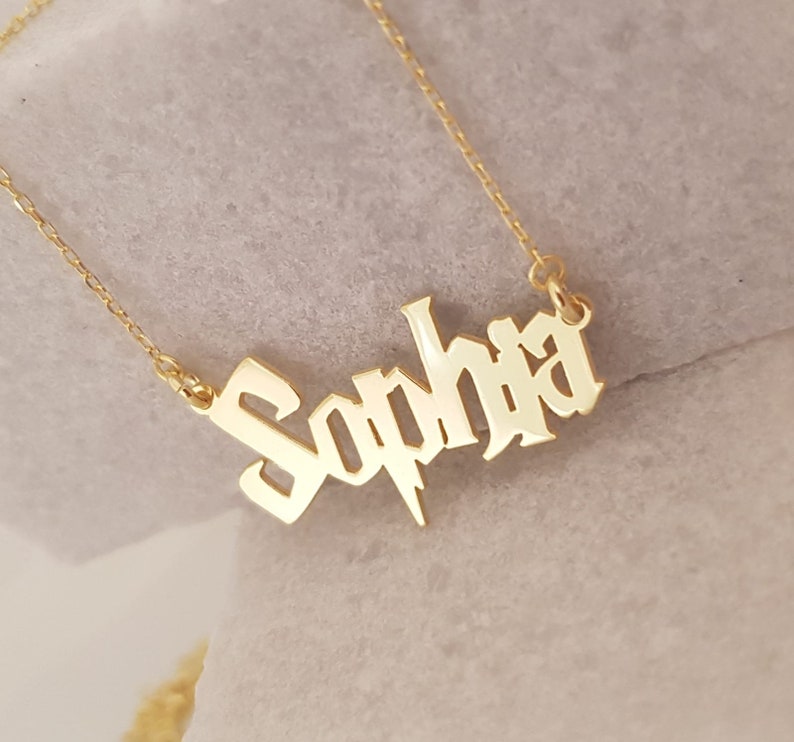 Puede incluir: Collar de oro con el nombre "Sophia" en fuente g&oacute;tica con un dise&ntilde;o de rayo.