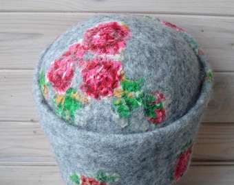 Pode incluir: Um chapéu de feltro cinza com um design floral com flores rosa e verdes. O chapéu está em uma cabeça de manequim de madeira.