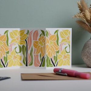 Daffodil Garland card featuring hand-carved linocut botanical portrait in yellow, green and pink. Double-sided concertina greeting card with bold, contemporary cottagecore design on eco-friendly recycled cardstock.