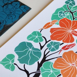 May include: A linocut print of a stylised floral design featuring orange, red, and teal flowers with green leaves. The print is on white paper.