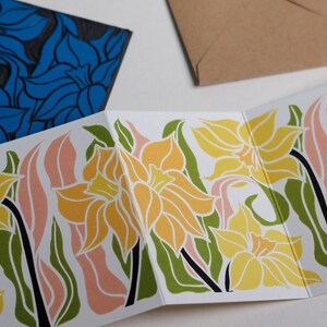 Hand-carved lino block shown beside finished Daffodil Garland card. Traditional linocut printmaking tools and original carved linoleum block displayed with a contemporary botanical portrait card. No AI, authentic craftsmanship from Norfolk studio