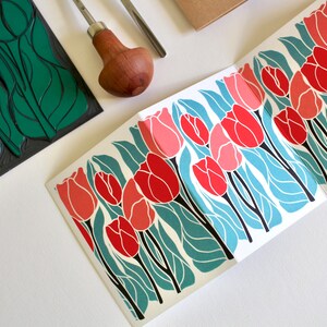 red and pink linocut tulips in a repeating pattern printed on to a folded concertina card