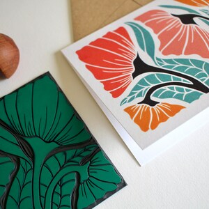 May include: Two cards with floral designs. One card features a green floral pattern, while the other card features a red, orange, and teal floral pattern. A wooden printing block with a green floral design is also shown.