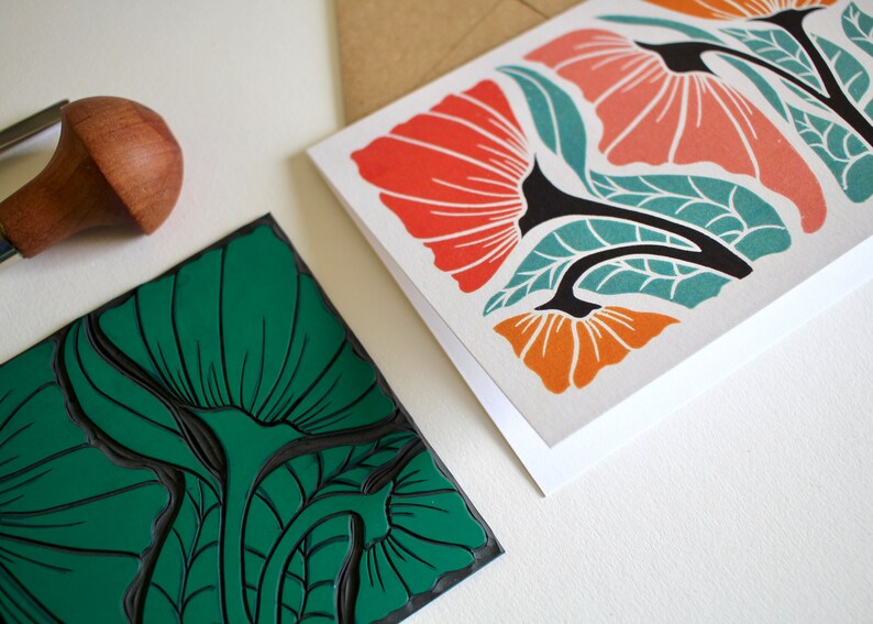 May include: Two cards with floral designs. One card features a green floral pattern, while the other card features a red, orange, and teal floral pattern. A wooden printing block with a green floral design is also shown.