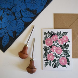 May include: A set of two wood handled carving tools with a card featuring a pink floral print. The card has a brown envelope.