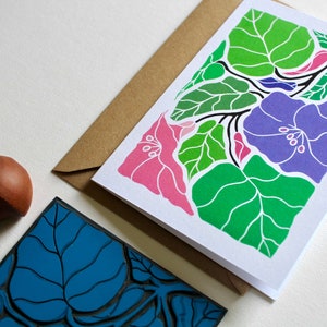 May include: A greeting card with a colorful floral design. The card features pink, purple, and green flowers with white outlines. The card is blank inside for writing a message.