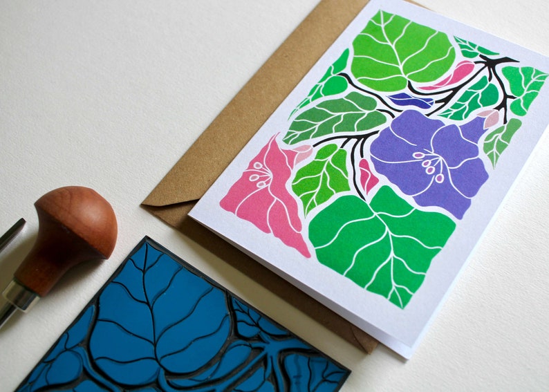 May include: A greeting card with a colorful floral design. The card features pink, purple, and green flowers with white outlines. The card is blank inside for writing a message.