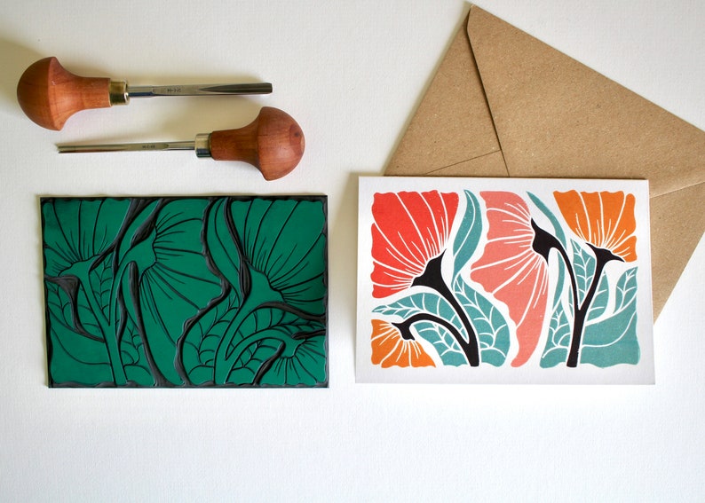 May include: A green linoleum block print of stylized flowers with a card showing the printed image in orange, red, and teal colors.