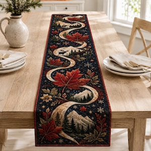 May include: A rectangular quilted table runner featuring a dark navy background with a winding cream-colored path, red maple leaves, snow-capped mountains, evergreen trees, moose silhouettes, and white snowflake patterns throughout the design.