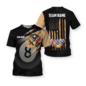 May include: Black t-shirt featuring a pool ball design with the number 8 and the text "YOUR NAME". The back of the shirt displays an American flag design with the text "TEAM NAME" above it. A pool ball rack is also featured.