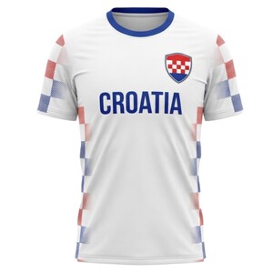 May include: White Croatia soccer jersey with blue trim on the collar and sleeves. The word "CROATIA" is printed in blue across the chest. The Croatian coat of arms is on the upper left chest, and red and blue checkered patterns are on the sleeves.