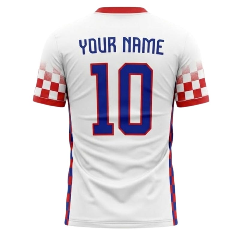 K&ouml;nnte beinhalten: Wei&szlig;es Fu&szlig;balltrikot mit roten und blauen Akzenten. Auf der R&uuml;ckseite ist die Nummer 10 in Blau mit roter Umrandung zu sehen, dar&uuml;ber steht der Text "YOUR NAME". Die &Auml;rmel haben ein rot-wei&szlig;es Schachbrettmuster.