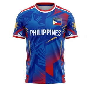 May include: Blue t-shirt with the word "PHILIPPINES" in white block letters. The shirt features a sun and star design, the Philippine flag, and the word "PILIPINAS". Red and yellow accents are on the sleeves and shoulders.
