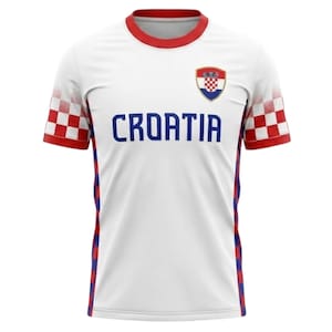 K&ouml;nnte beinhalten: Wei&szlig;es Kroatien-Fu&szlig;balltrikot mit roten und blauen Akzenten. Das Trikot zeigt den Schriftzug "CROATIA" in Blau, das kroatische Wappen und rot-wei&szlig; karierte Muster auf den &Auml;rmeln.