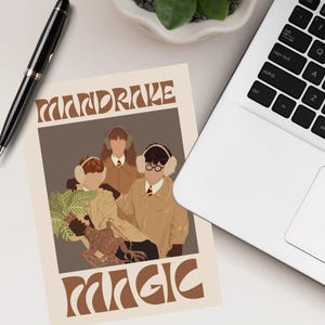 Peut inclure: Une affiche beige avec les mots "MANDRAKE MAGIC" en lettres marron. L'affiche présente une illustration de trois personnages portant des cache-oreilles et des manteaux beiges. Un stylo noir et un ordinateur portable sont visibles.